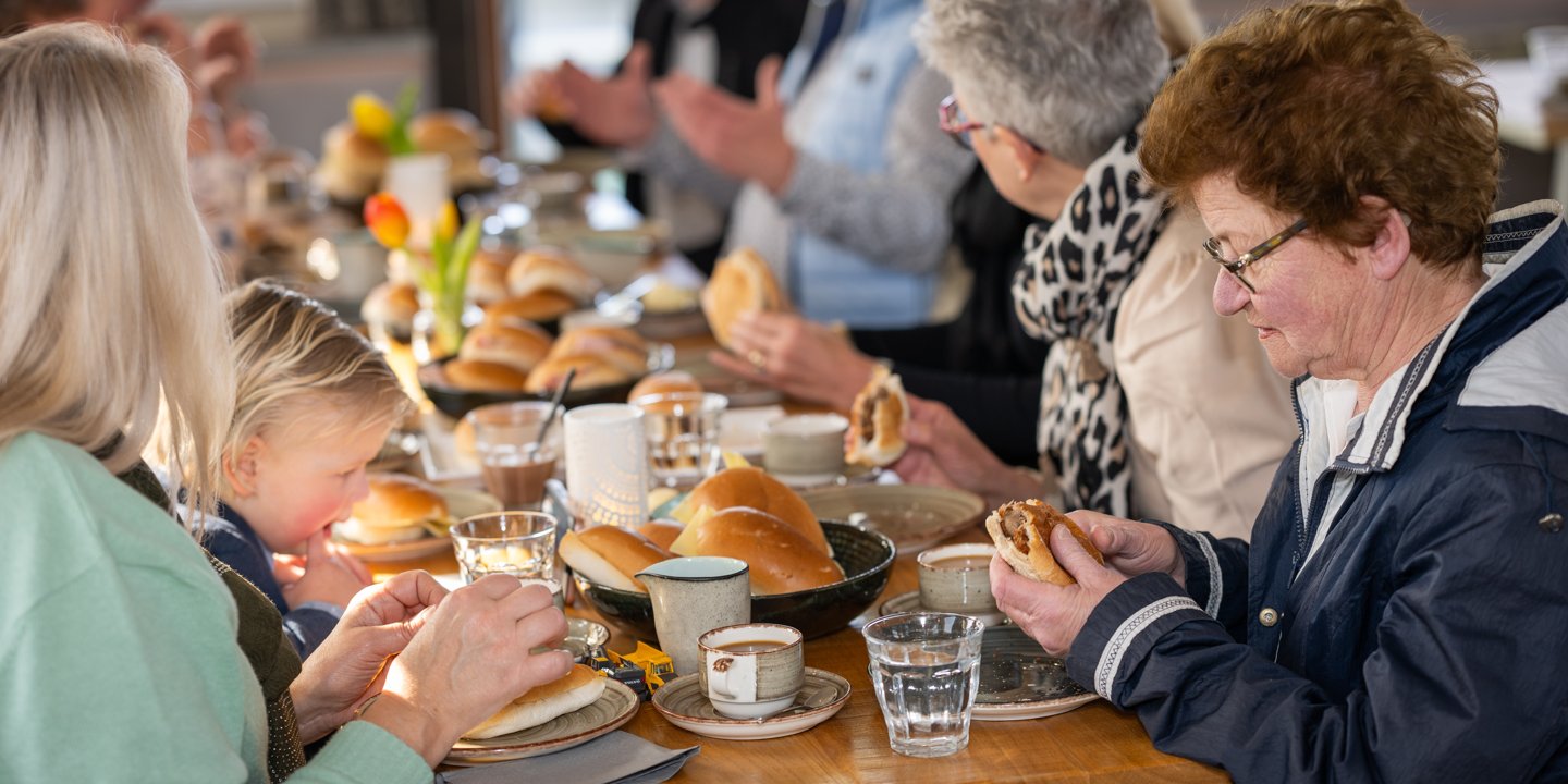 Een kind en volwassen gasten samen aan de lunchtafel in de salon