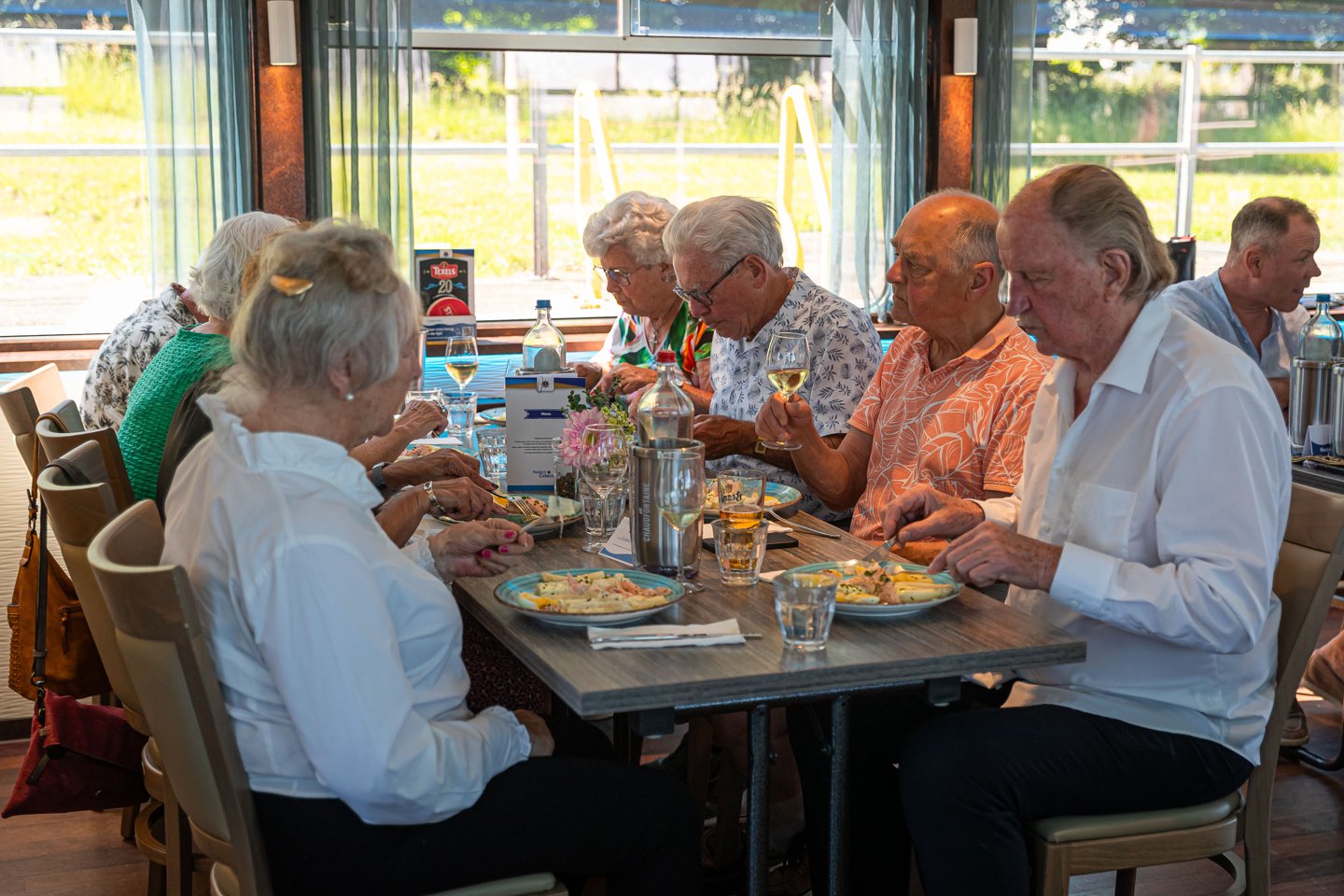 Gasten zitten rond een lange tafel naast de ramen van het schip